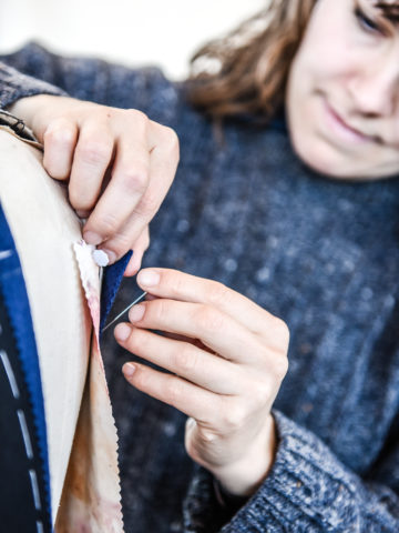 The image shows a student learning to tailor a bespoke jacket